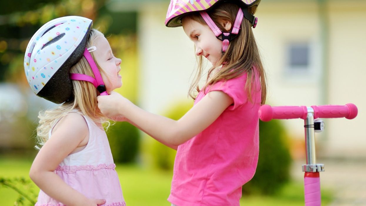 A big sister helps her younger sibling on with a helmet.