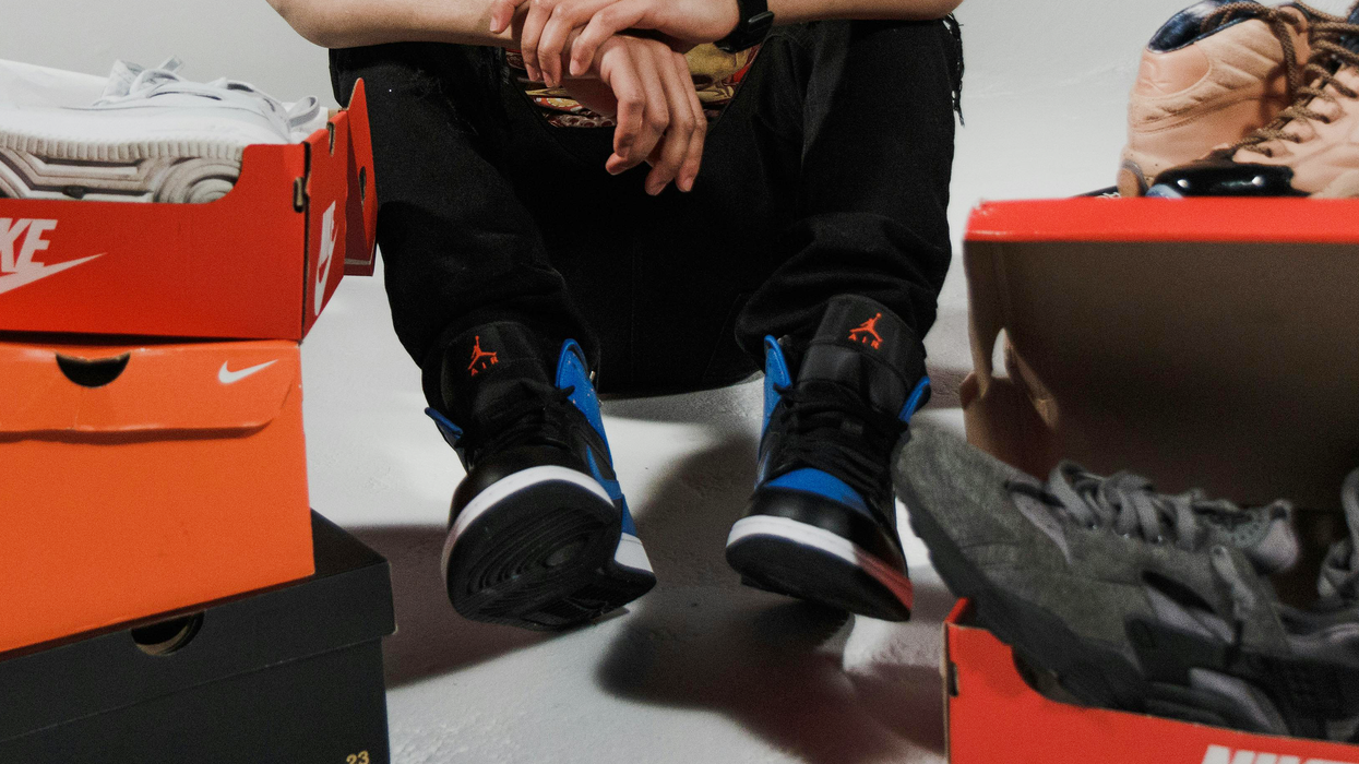 A boy sits among a collection of shoes.
