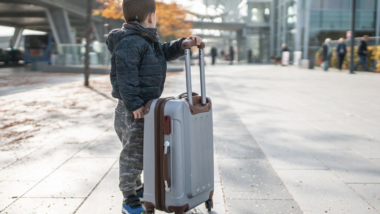 A boy standing beside a suitcase nearly as large as himself.