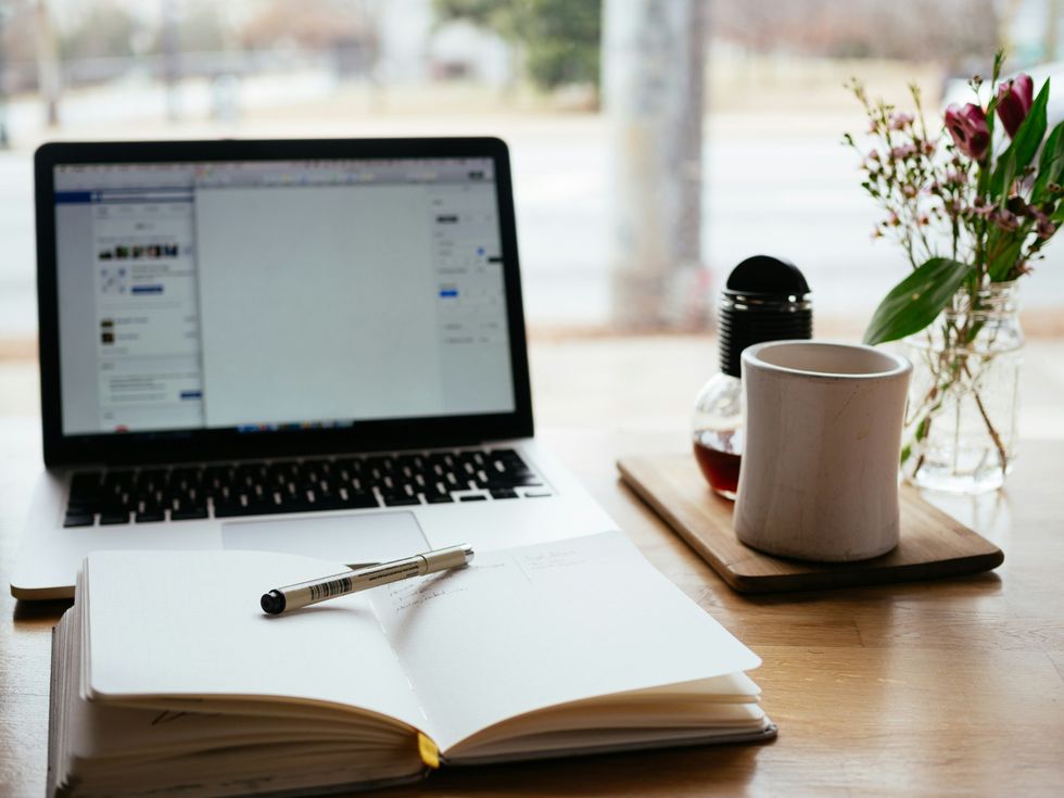 A computer open in front of a blank notebook. And there's also a cup of tea and honey on the table.