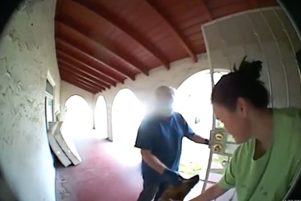 A man and woman pet a dog at her front door.