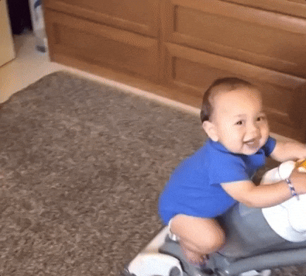 GIF of a baby riding on a vacuum and laughing