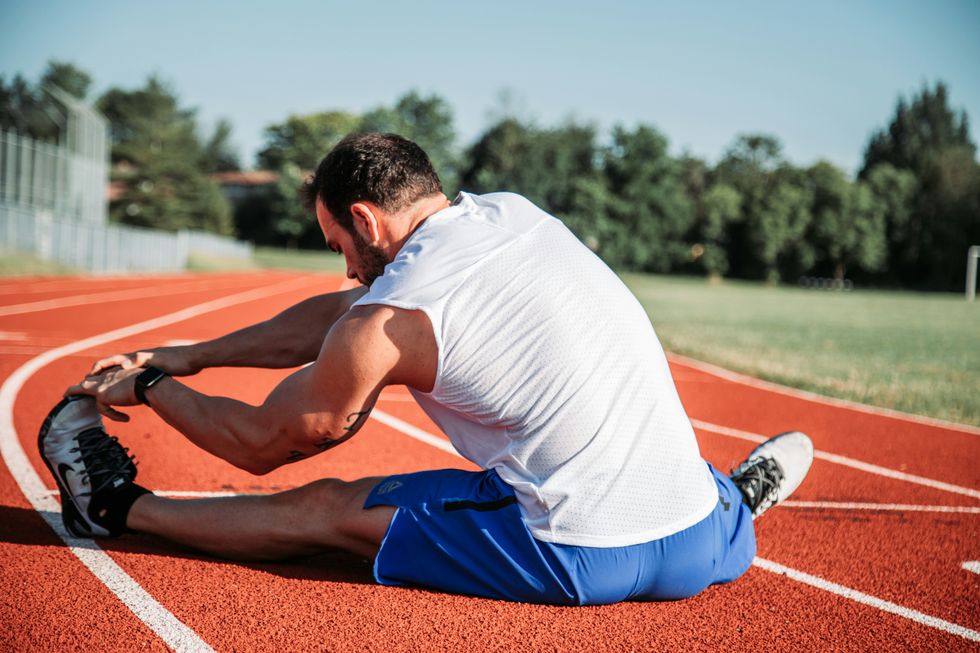 man in white sleeveless top stretching before a run on the track