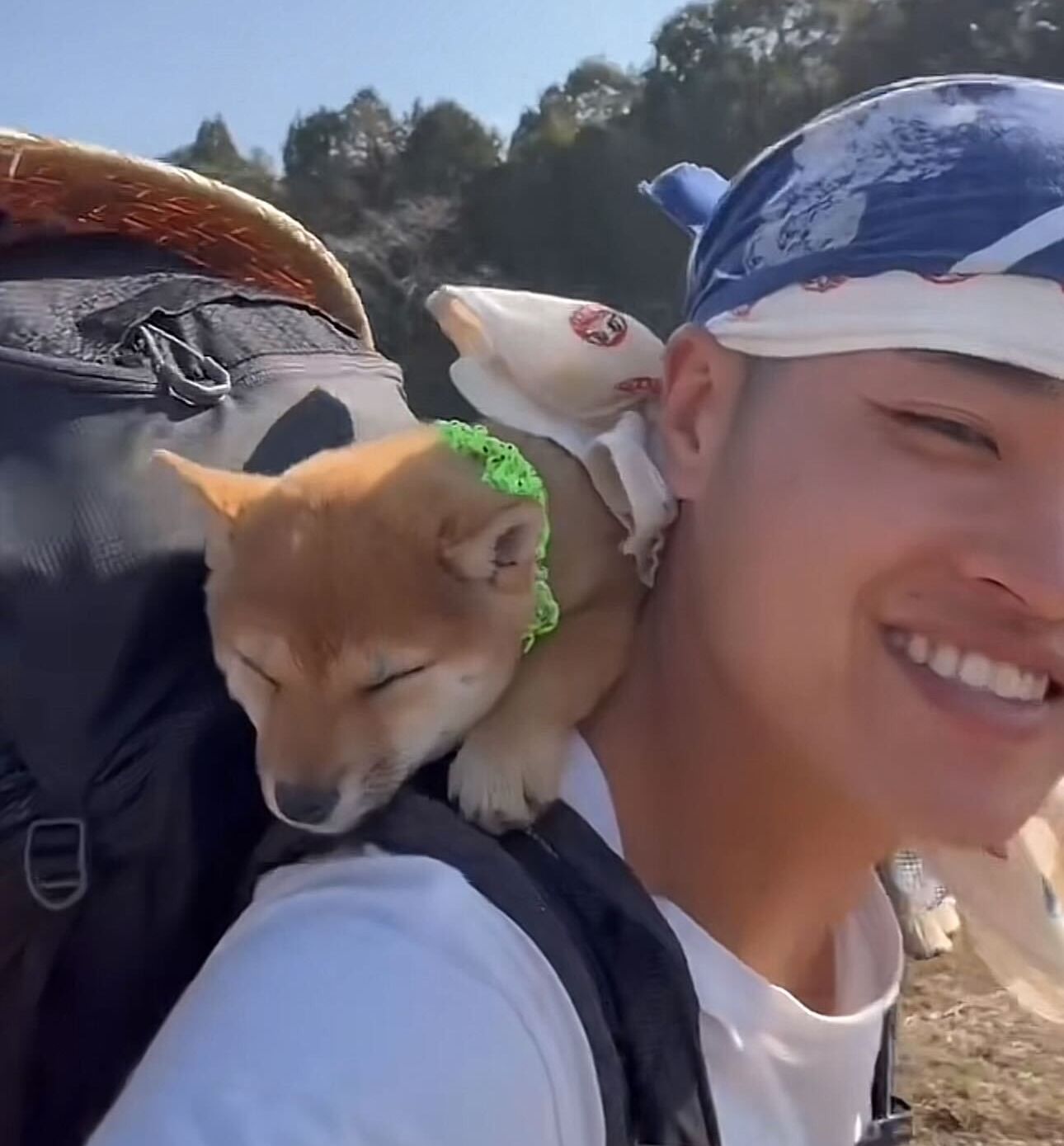 Man smiling at camera, sleeping Shiba Inu puppy resting in his camping backpack
