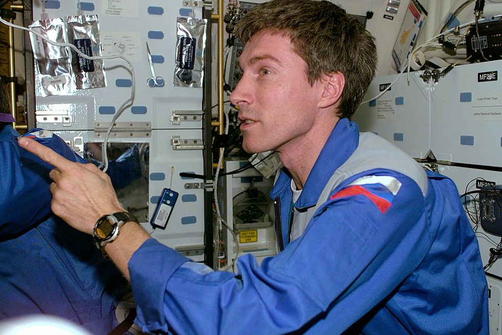 Sergei Krikalev floating inside the space station, speaking into a microphone with equipment and control panels around him.